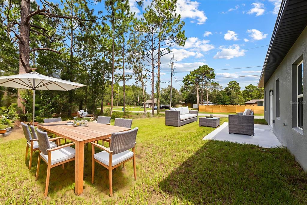 A backyard features a wooden dining set with an umbrella and a patio seating area — 1071 W HAMPSHIRE BOULEVARD, DUNNELLON, FL