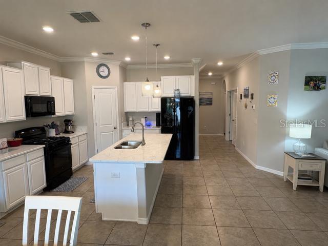 A kitchen features white cabinets, a central island with a sink, and black appliances — 8913 FLOURISH DRIVE, LAND O LAKES, FL