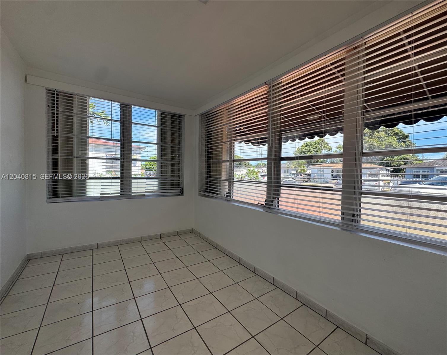 An empty sunroom features white tiled floors, white walls, and large windows with horizontal blinds — 459 SE 3rd St, Hialeah FL 33010, HIALEAH, FL
