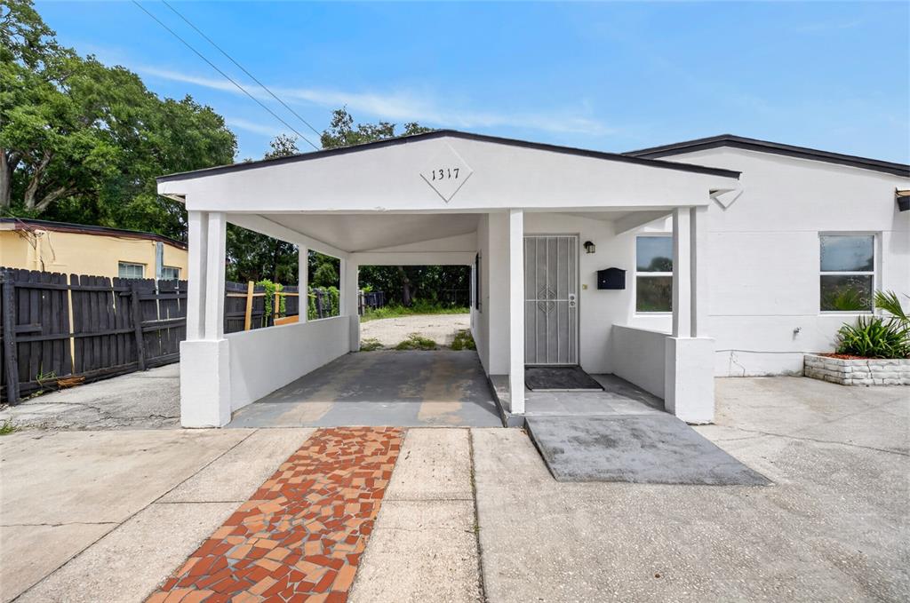 A white house exterior features a covered carport, a front entrance, and a paved driveway — 1317 N PINE HILLS ROAD, ORLANDO, FL