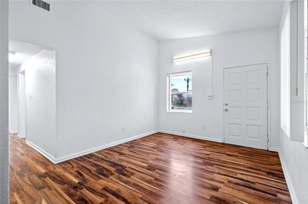 An empty room features white walls, wood-look flooring, a single window, and a white door — 1317 N PINE HILLS ROAD, ORLANDO, FL