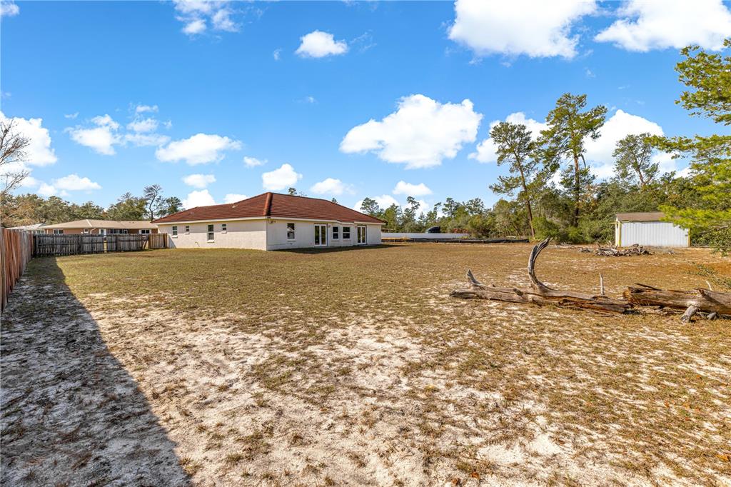 A large, sandy backyard features a single-story house, a small shed, and a fallen log — 17179 SW 41ST CIRCLE, OCALA, FL