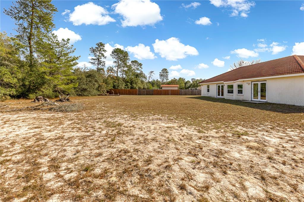 A large, sandy backyard sits behind a house with a red tiled roof — 17179 SW 41ST CIRCLE, OCALA, FL