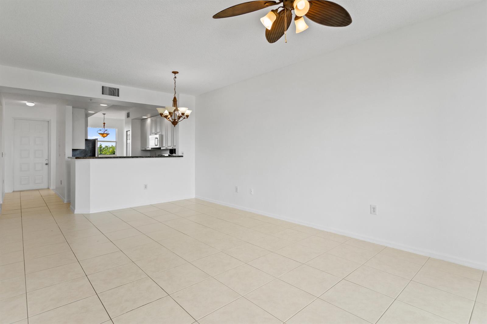 An empty room with beige tile flooring, white walls, a ceiling fan, and a kitchen pass-through — 27 Royal Palm Way # 503, Boca Raton FL 33432, BOCA RATON, FL