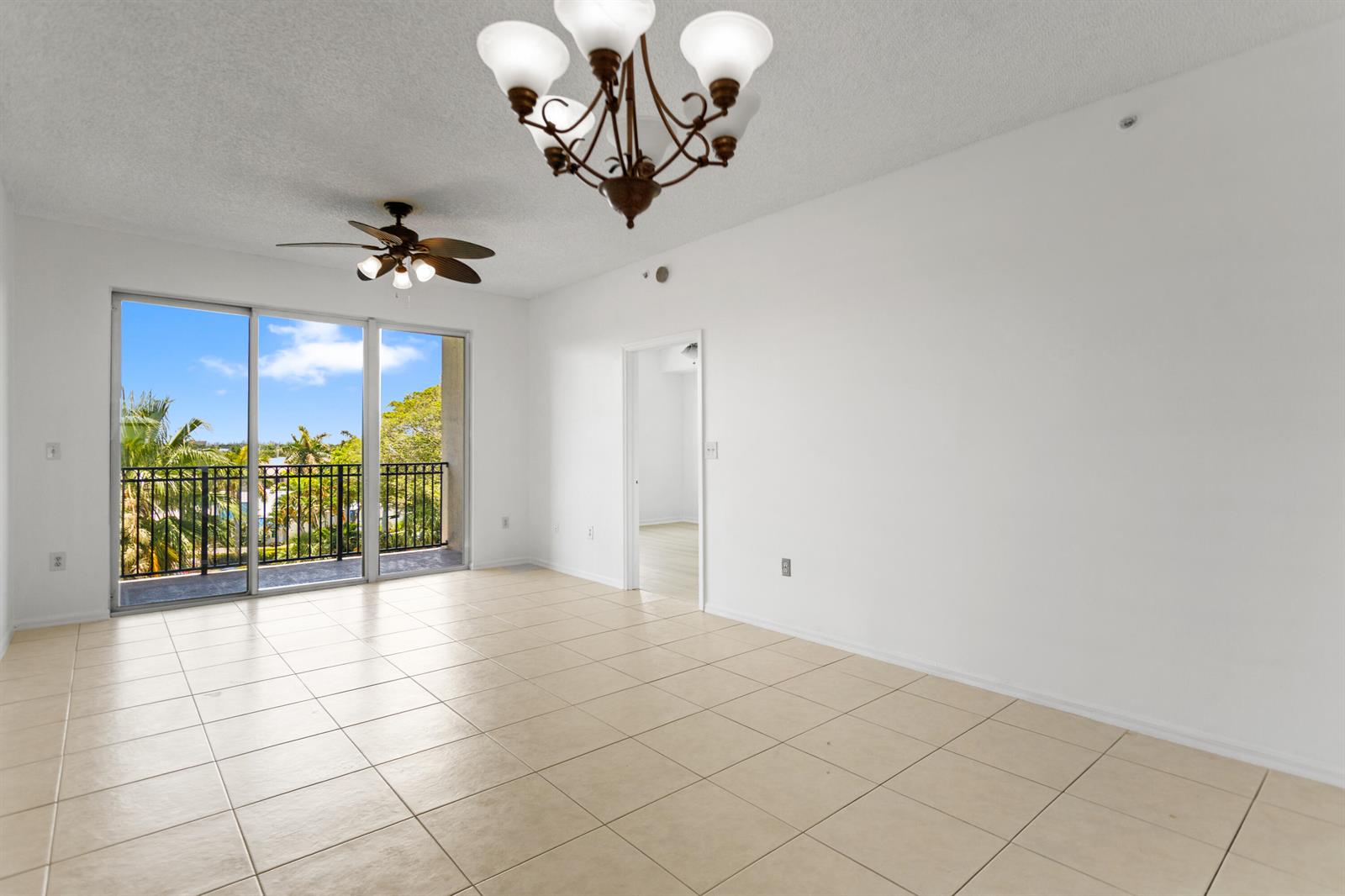 An empty room with beige tile flooring, a ceiling fan, a chandelier, and sliding glass doors — 27 Royal Palm Way # 503, Boca Raton FL 33432, BOCA RATON, FL