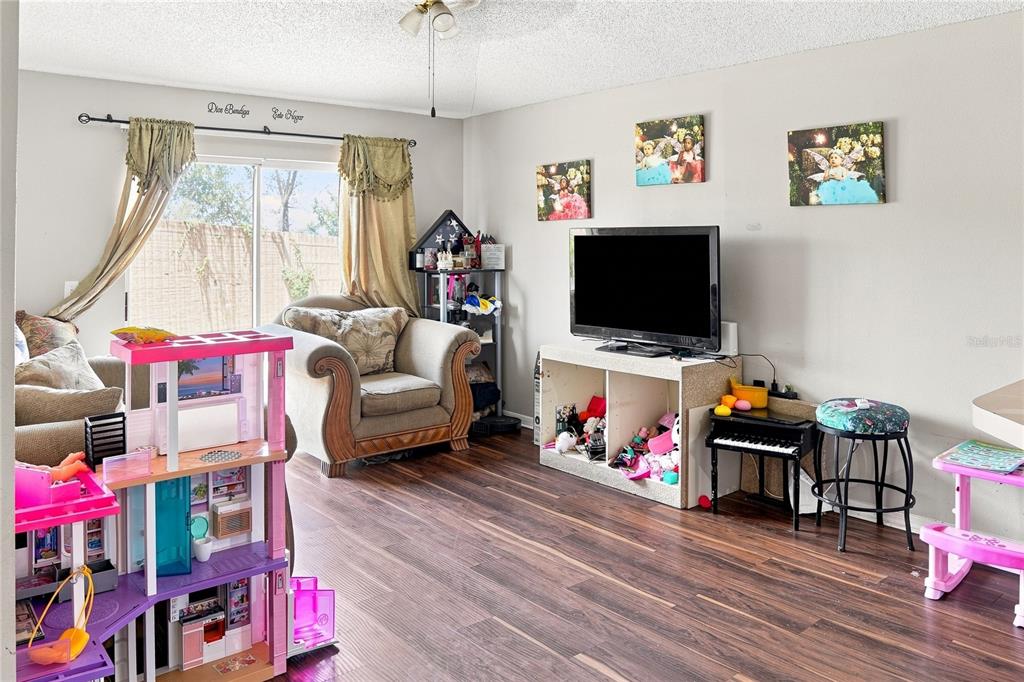 A living room features wood-look flooring, a television on a storage unit, and a dollhouse — 4243 MENDENWOOD LANE, ORLANDO, FL