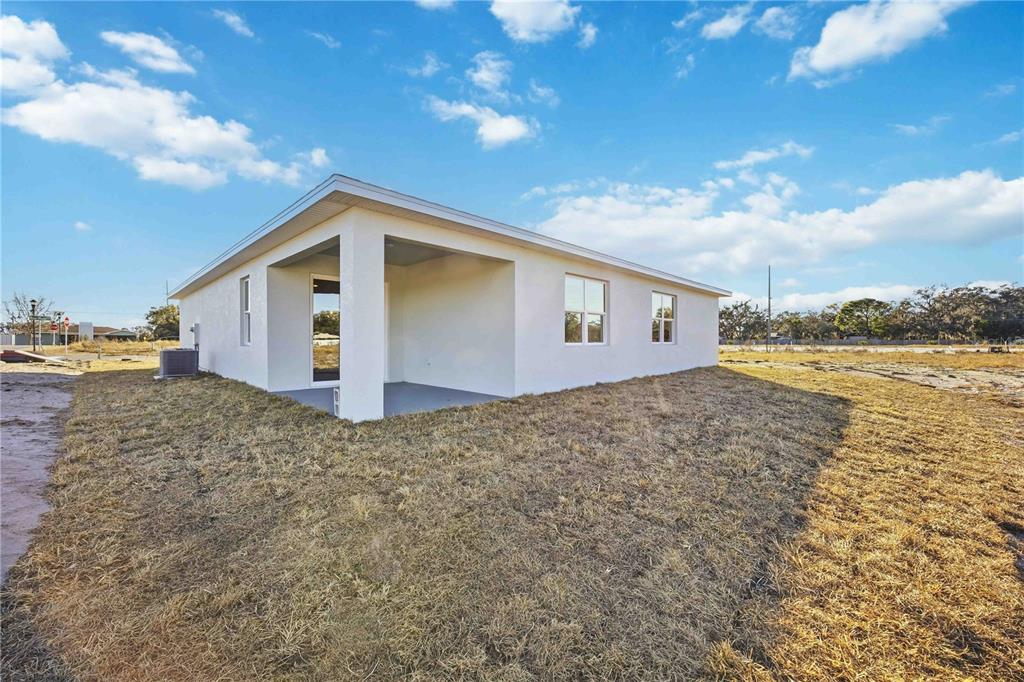 The exterior of a white stucco house features a covered patio and a grassy yard — 2145 RIVER HAWK LOOP, WINTER HAVEN, FL