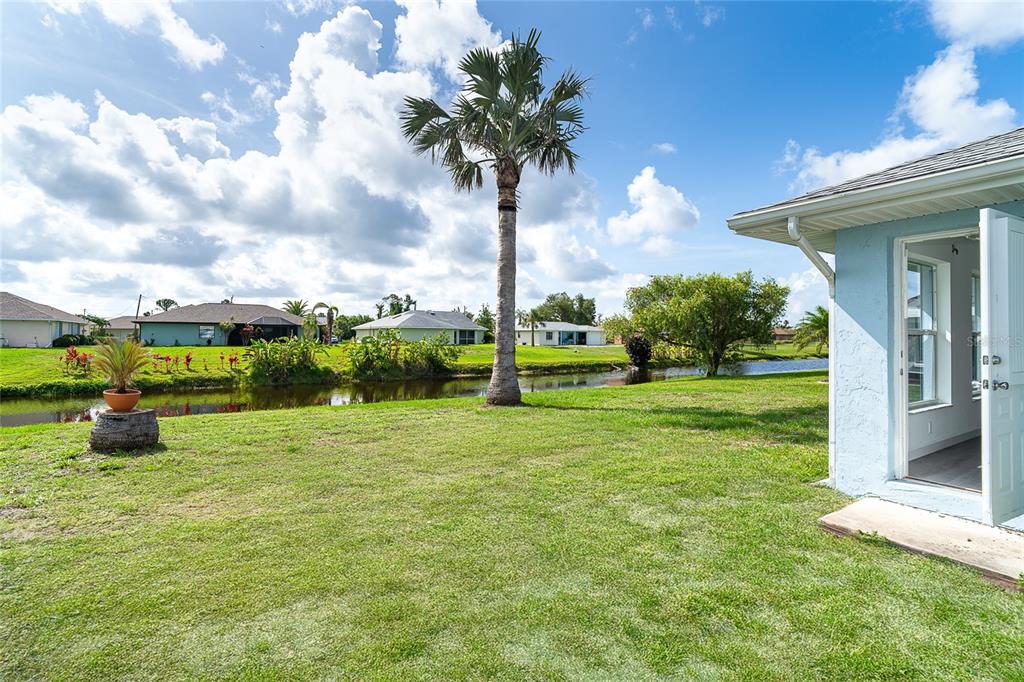 A grassy backyard features a tall palm tree, a small canal, and a light blue house — 15 BUNKER PLACE, ROTONDA WEST, FL