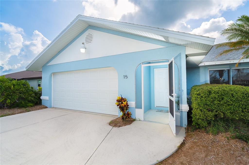 A light blue house exterior features a white garage door, a front entrance, and landscaping — 15 BUNKER PLACE, ROTONDA WEST, FL