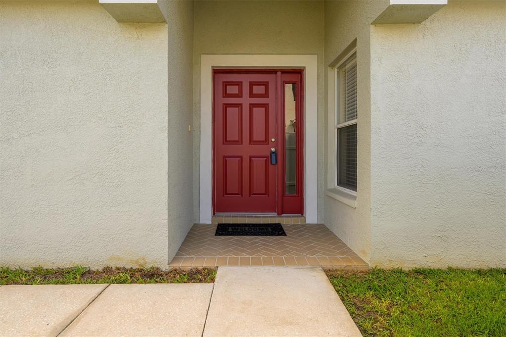 A red front door with a side window sits under a covered entryway — 25831 SYME COURT, LAND O LAKES, FL