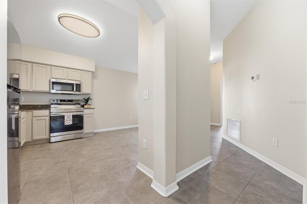 A kitchen with light-colored cabinets and stainless steel appliances opens into a tiled hallway — 25831 SYME COURT, LAND O LAKES, FL