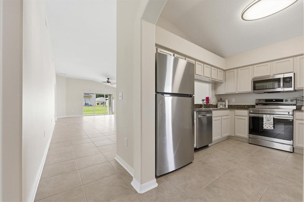 A kitchen with stainless steel appliances and cream cabinets opens to a tiled living area — 25831 SYME COURT, LAND O LAKES, FL