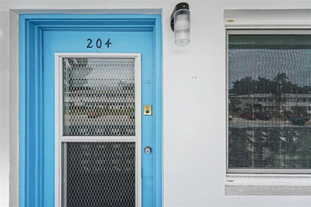 A bright blue front door with a screen door and the number 204 sits beside a window — 8555 112TH STREET N UNIT 204, SEMINOLE, FL