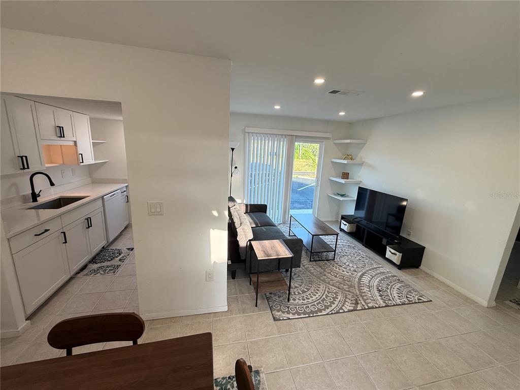 A kitchen with white cabinets opens into a living room featuring a sofa and television — 146 BOUNDARY BOULEVARD UNIT B 102, ROTONDA WEST, FL