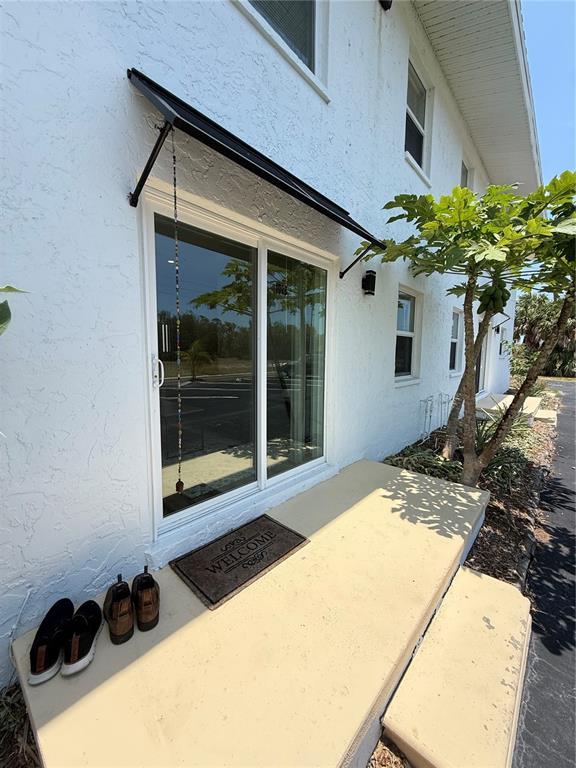 A white exterior wall features a sliding glass door, a metal awning, and concrete steps — 146 BOUNDARY BOULEVARD UNIT B 102, ROTONDA WEST, FL