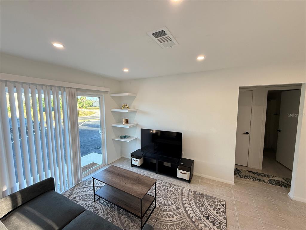 A living room features a sliding glass door, floating shelves, a television, and tile flooring — 146 BOUNDARY BOULEVARD UNIT B 102, ROTONDA WEST, FL