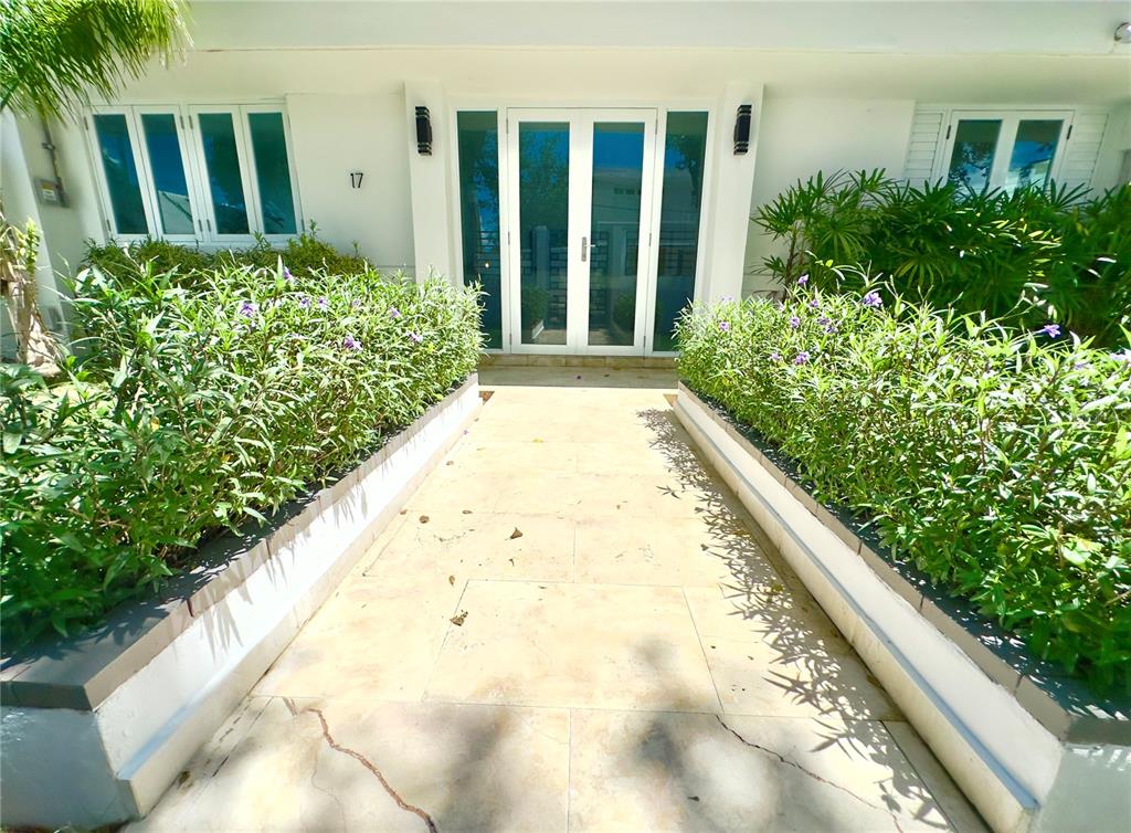 A paved walkway leads to the white double-door entrance of a building with landscaped planters — 17 GUERRERO NOBLE, SAN JUAN, PR
