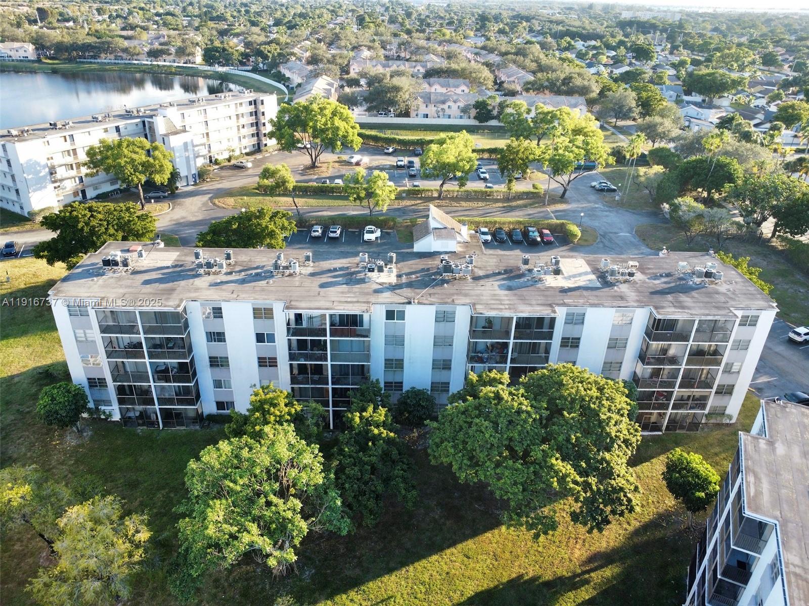 An aerial view shows a multi-story apartment building with a parking lot and trees — 8730 N Sherman Cir # 407, Miramar FL 33025, MIRAMAR, FL