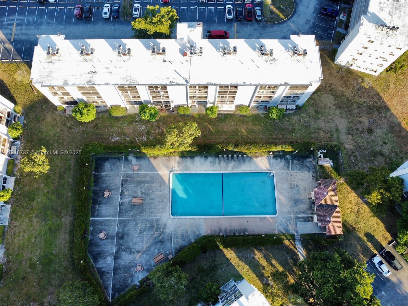 An aerial view shows a rectangular apartment building next to a swimming pool and parking — 8730 N Sherman Cir # 407, Miramar FL 33025, MIRAMAR, FL