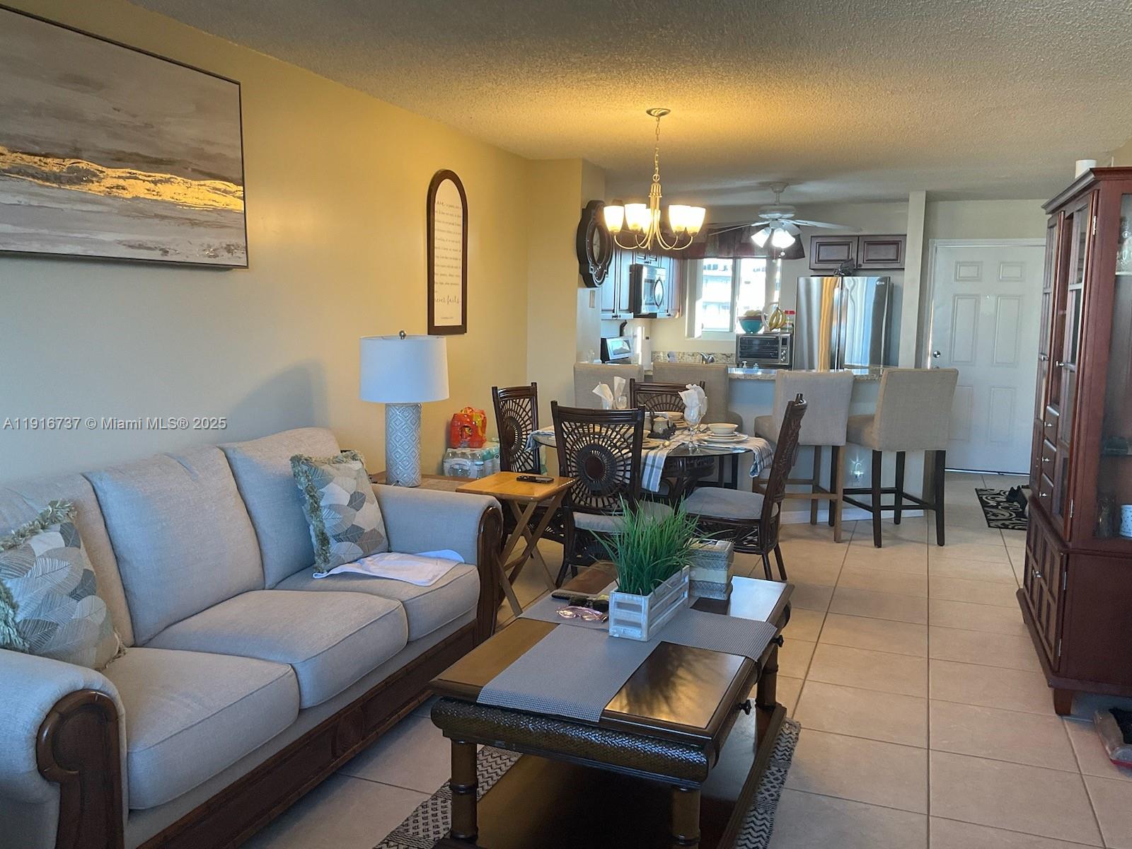A living room and dining area feature tile flooring, a beige sofa, and kitchen access — 8730 N Sherman Cir # 407, Miramar FL 33025, MIRAMAR, FL