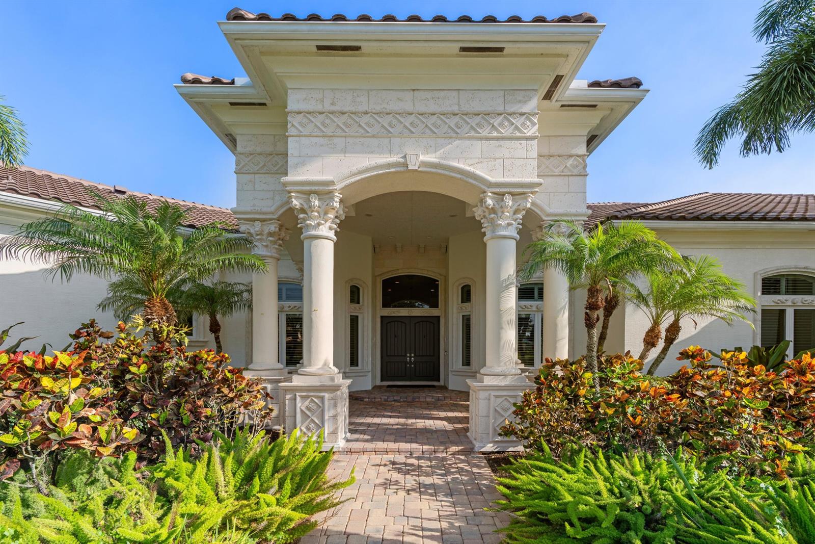 A stone-columned entryway leads to a dark double-door entrance of a Mediterranean-style home — 15885 Boeing Court, Wellington FL 33414, WELLINGTON, FL