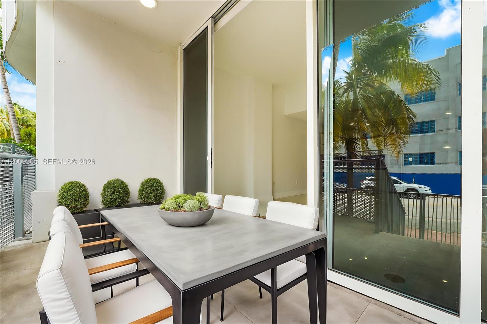 A modern outdoor dining area features a concrete table and white chairs on a balcony — 2100 Park Ave # 108, Miami Beach FL 33139, MIAMI BEACH, FL