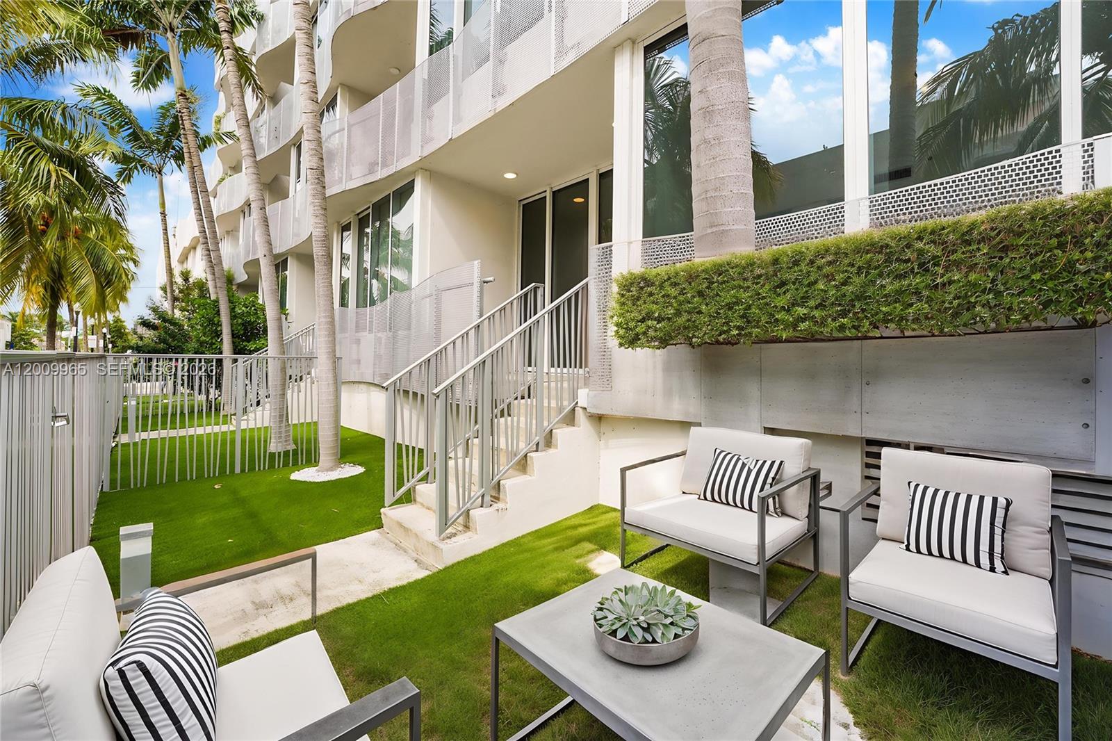 A patio area features outdoor furniture on artificial grass with stairs leading to a building entrance — 2100 Park Ave # 108, Miami Beach FL 33139, MIAMI BEACH, FL