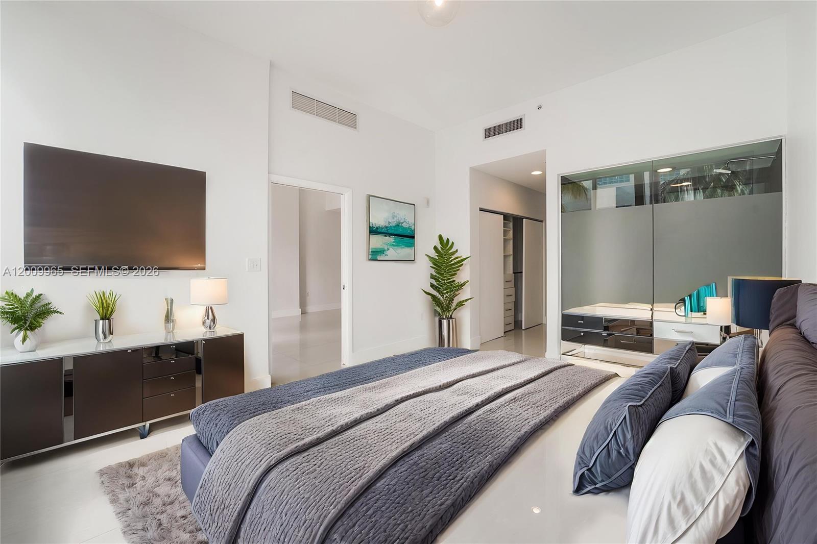 A modern bedroom features a large bed, a wall-mounted television, and a glass-enclosed bathroom — 2100 Park Ave # 108, Miami Beach FL 33139, MIAMI BEACH, FL