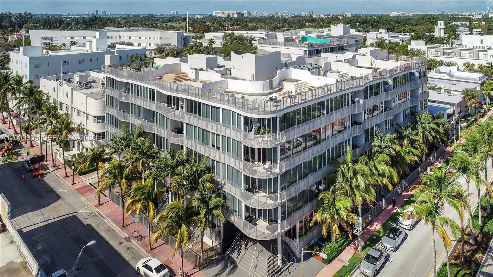 An aerial view of a modern, multi-story apartment building with curved glass balconies and palm trees — 2100 Park Ave # 108, Miami Beach FL 33139, MIAMI BEACH, FL