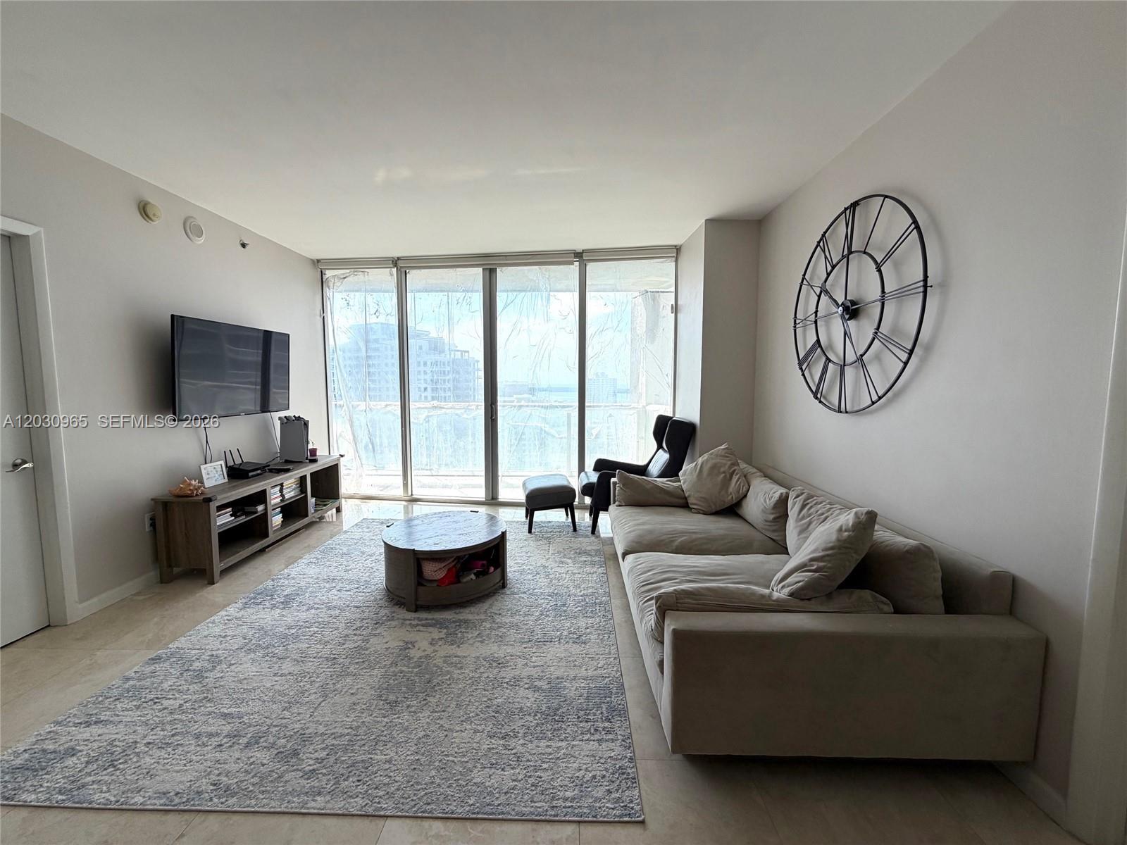 A living room features a large area rug, a sectional sofa, and a wall-mounted clock — 475 Brickell ave # 2707, Miami FL 33131, MIAMI, FL