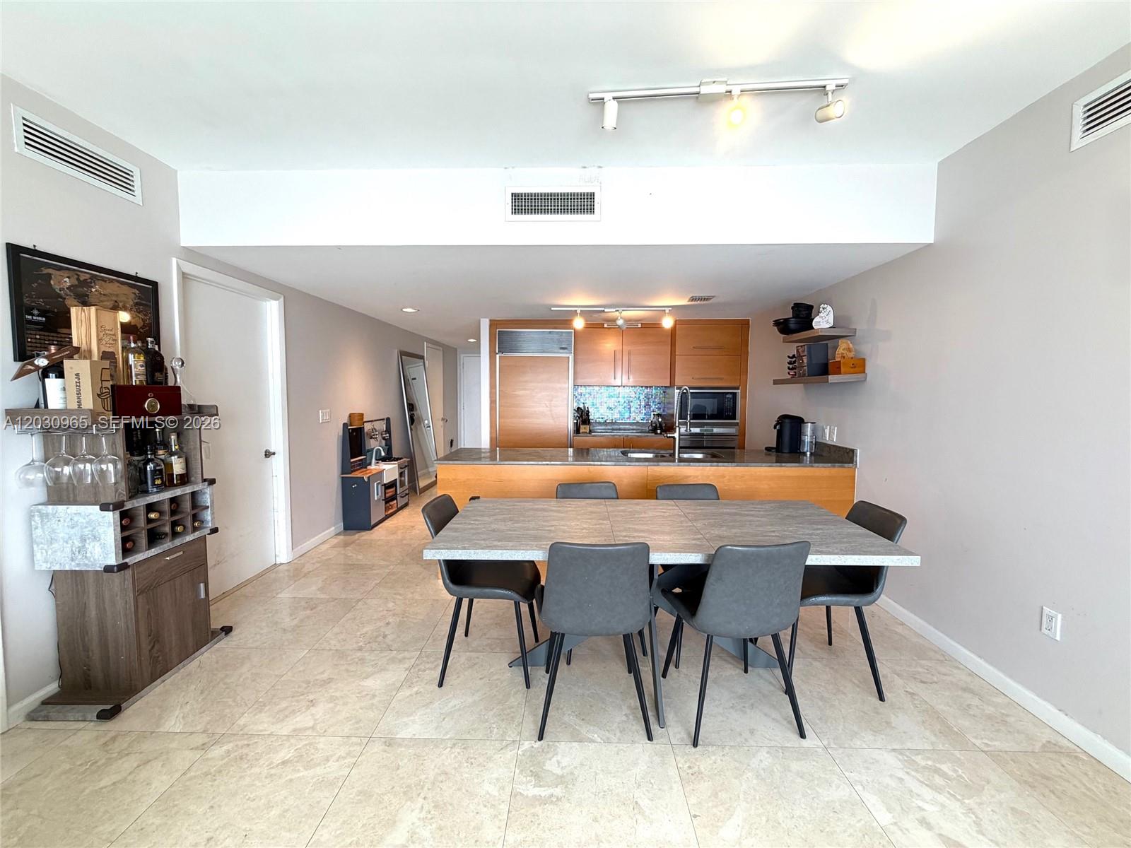 A dining area with a grey table and chairs sits before an open-concept kitchen — 475 Brickell ave # 2707, Miami FL 33131, MIAMI, FL