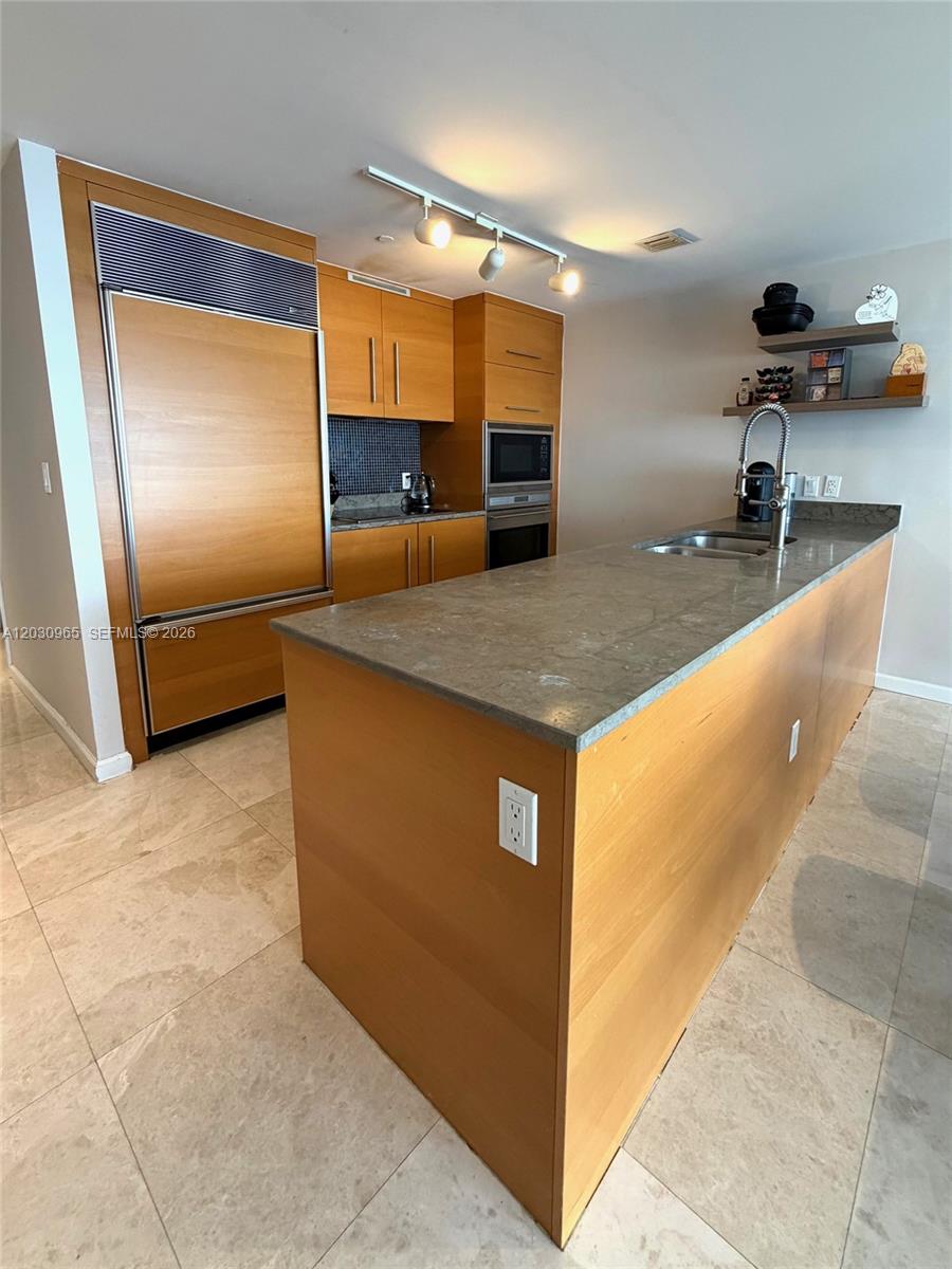 A modern kitchen features light wood cabinetry, a stone island countertop, and tile flooring — 475 Brickell ave # 2707, Miami FL 33131, MIAMI, FL