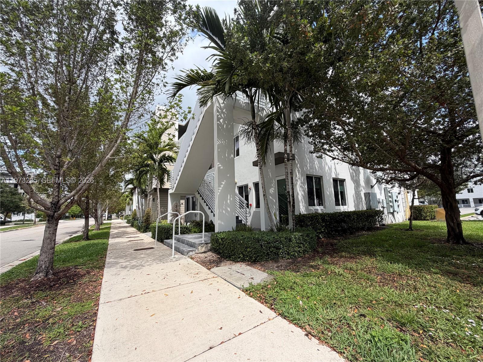 A white multi-story building exterior features an outdoor staircase and surrounding palm trees — 6401 NW 103rd Pl # 106, Doral FL 33178, DORAL, FL