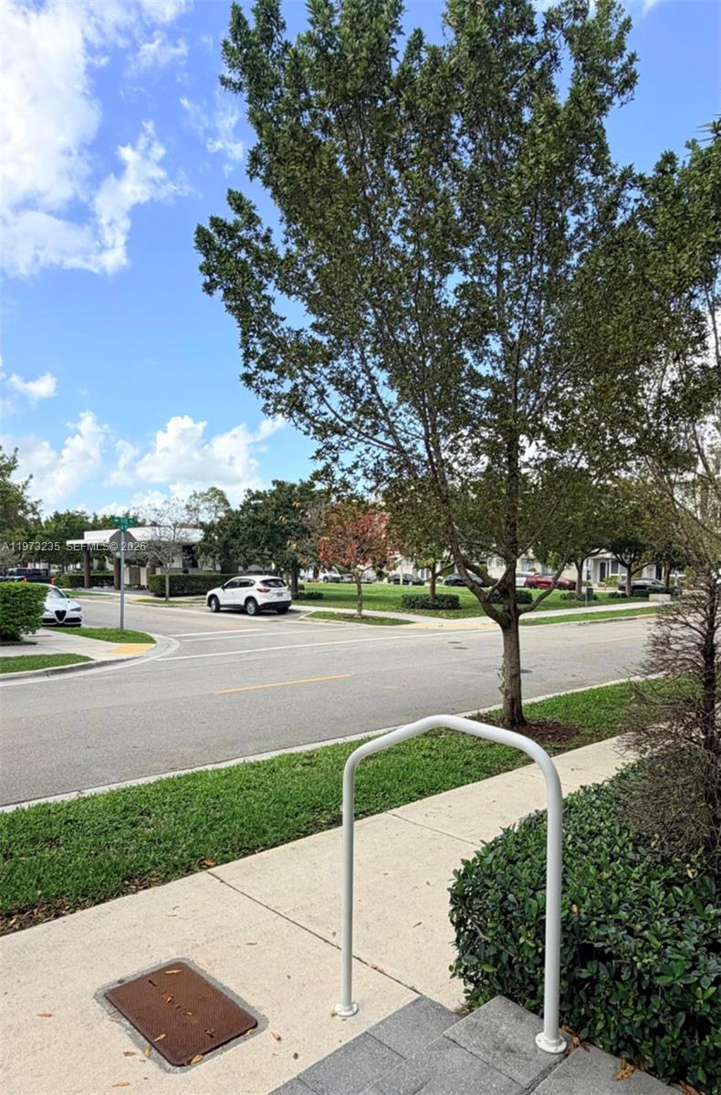 A view of a suburban street intersection with trees, sidewalks, and parked cars — 6401 NW 103rd Pl # 106, Doral FL 33178, DORAL, FL