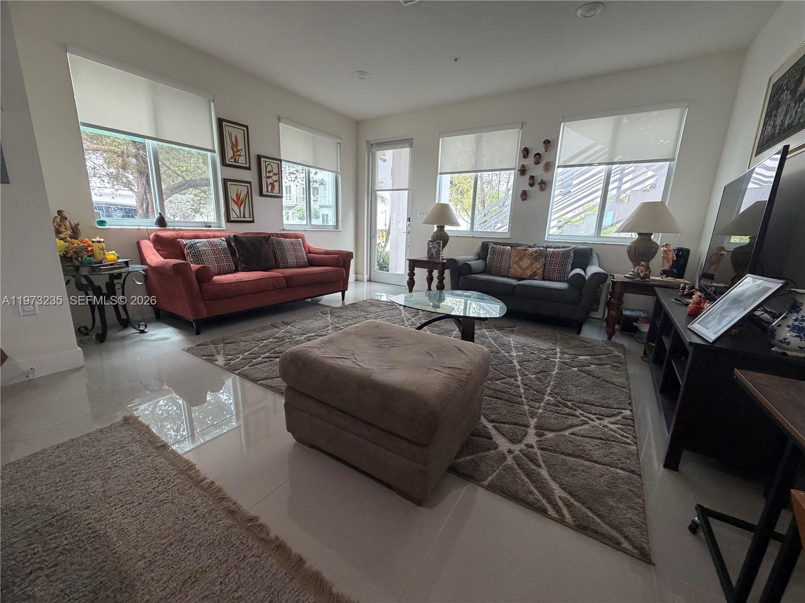 A living room features a red sofa, a grey sofa, an ottoman, and tile flooring — 6401 NW 103rd Pl # 106, Doral FL 33178, DORAL, FL