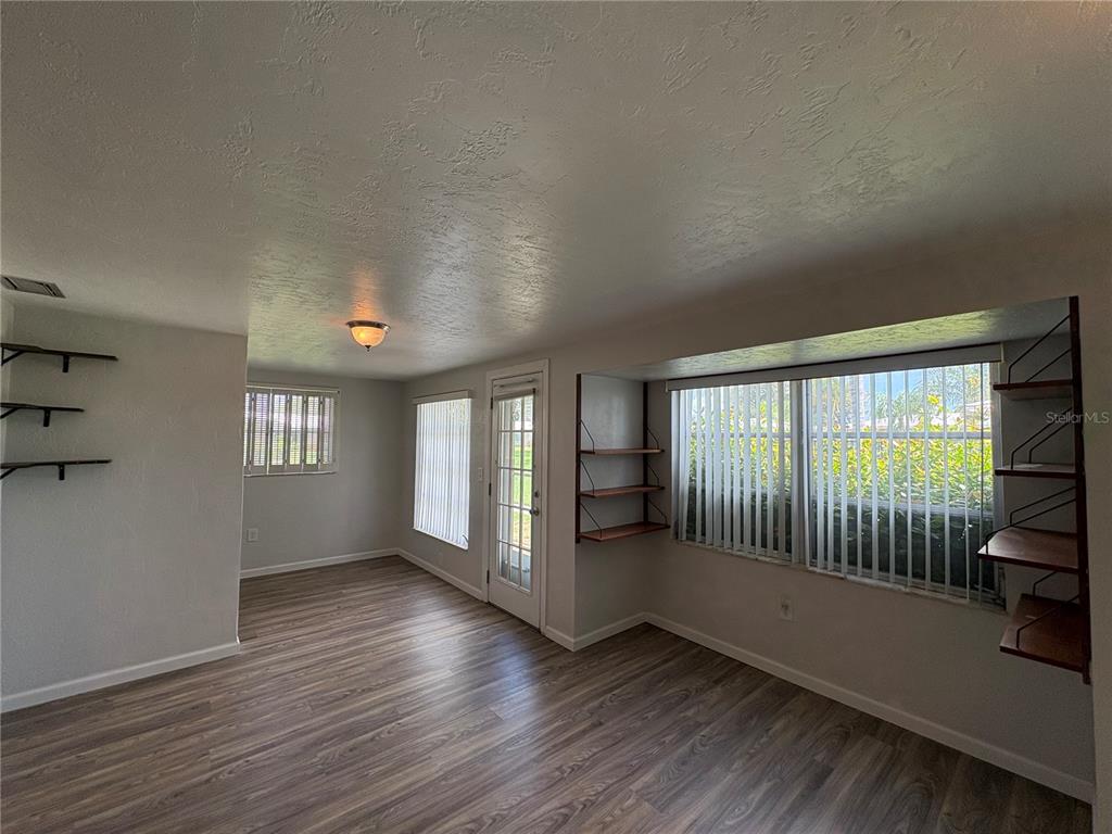 A room with wood-look flooring, built-in wall shelving, vertical blinds, and a glass-paneled exterior door — 3276 BRUNSWICK LANE UNIT 705, SARASOTA, FL
