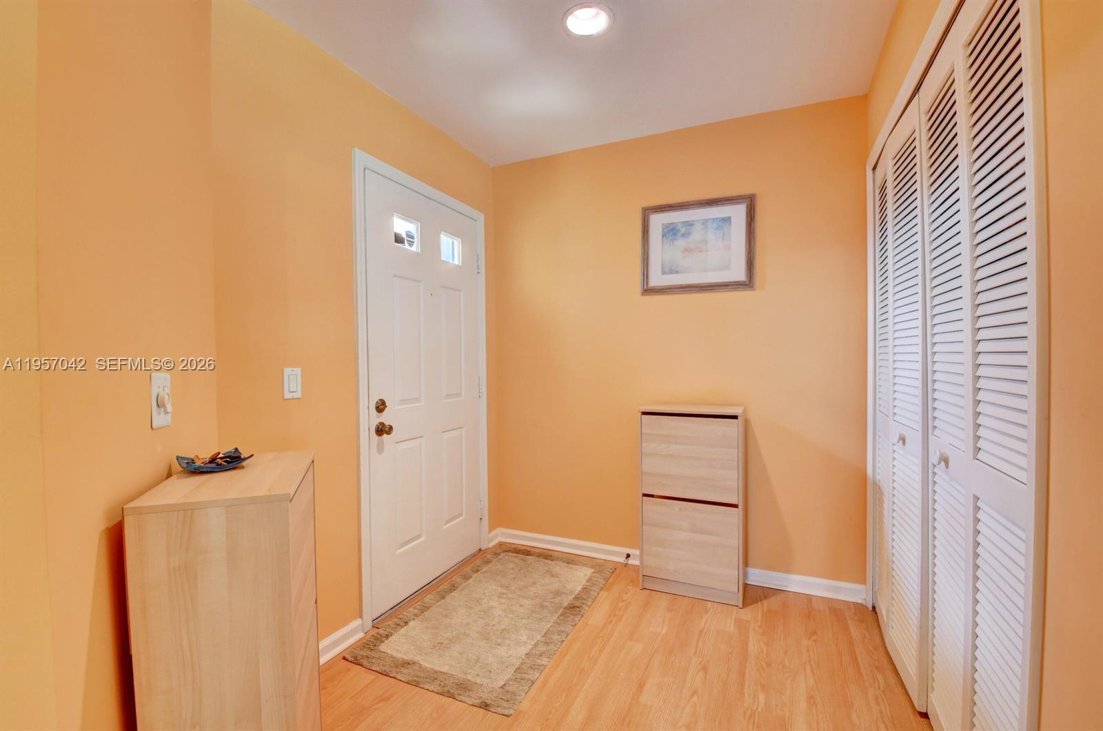 An entryway features orange walls, light wood flooring, a white door, and louvered closet doors — 6027 Parkwalk Dr # 0, Boynton Beach FL 33472, BOYNTON BEACH, FL