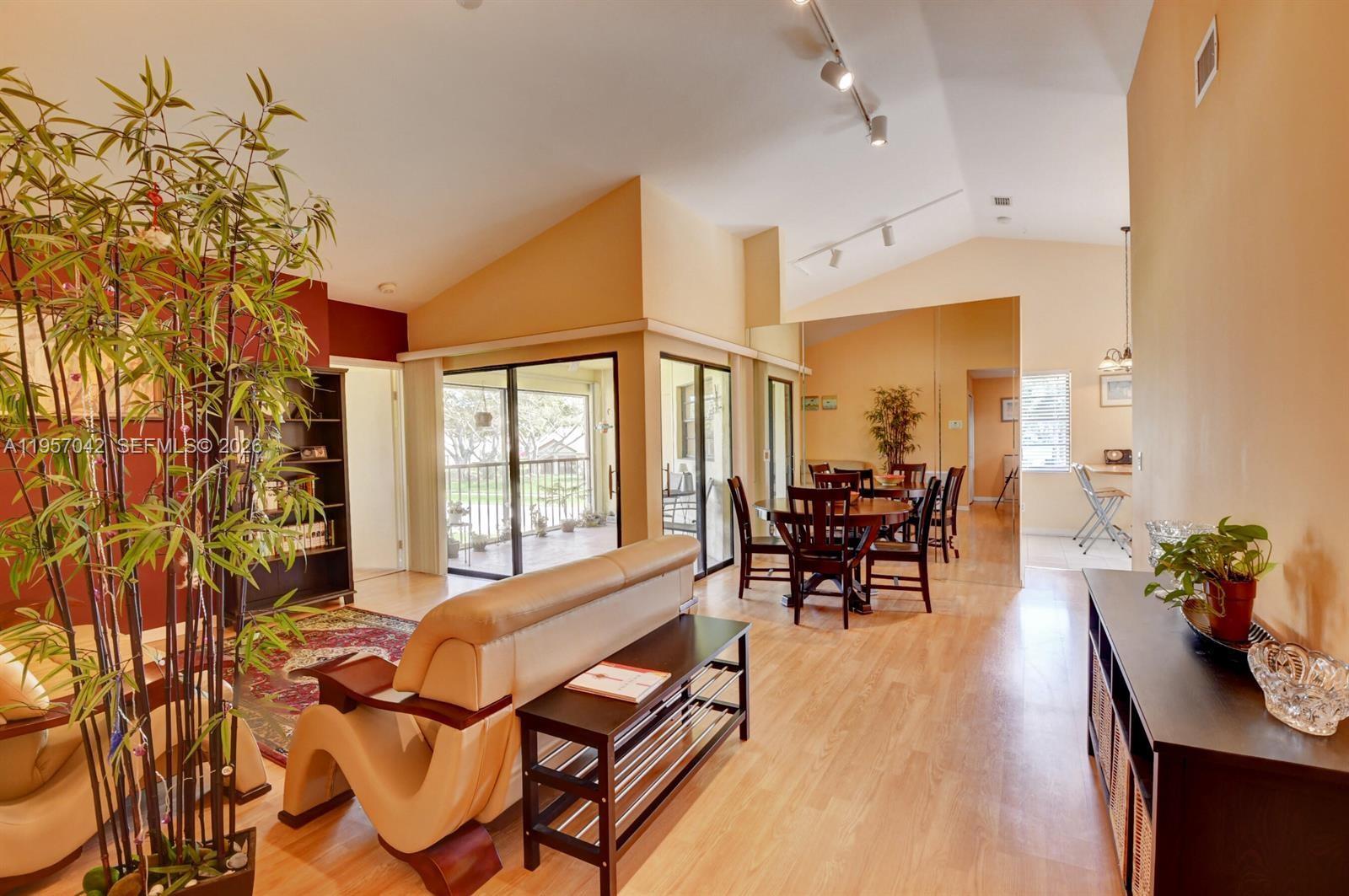 A living and dining area with vaulted ceilings, wood-look flooring, and a mirrored wall — 6027 Parkwalk Dr # 0, Boynton Beach FL 33472, BOYNTON BEACH, FL