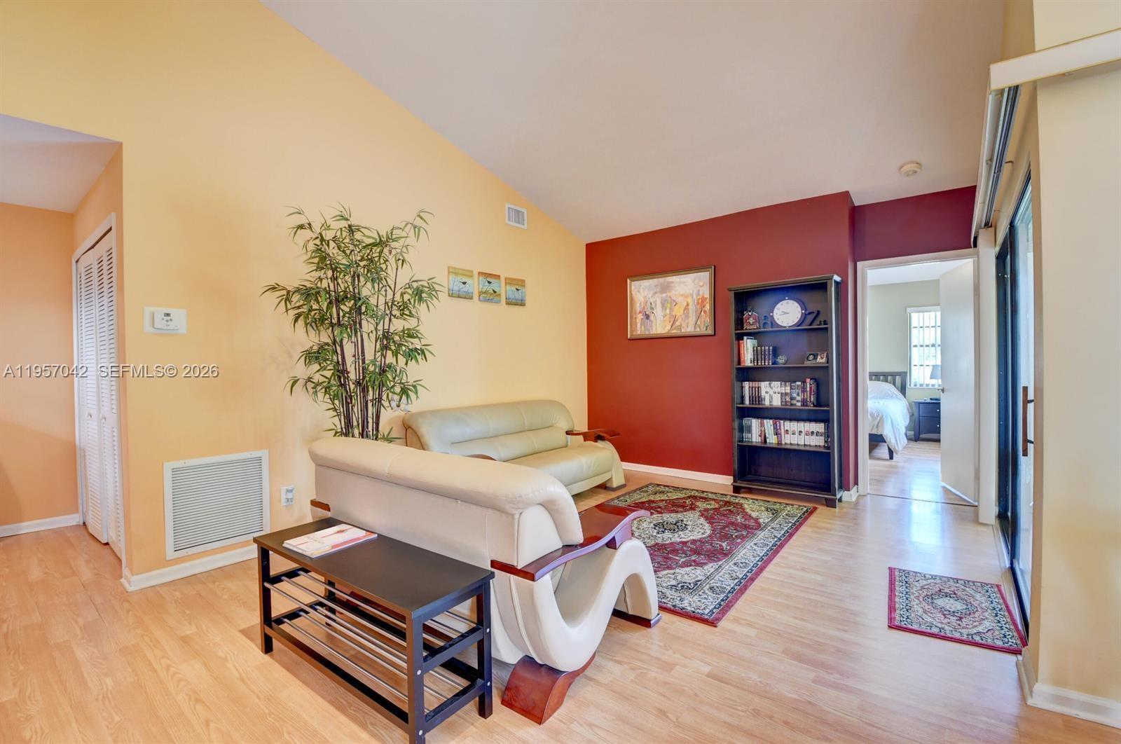 A living room features light wood floors, a red accent wall, and two leather sofas — 6027 Parkwalk Dr # 0, Boynton Beach FL 33472, BOYNTON BEACH, FL