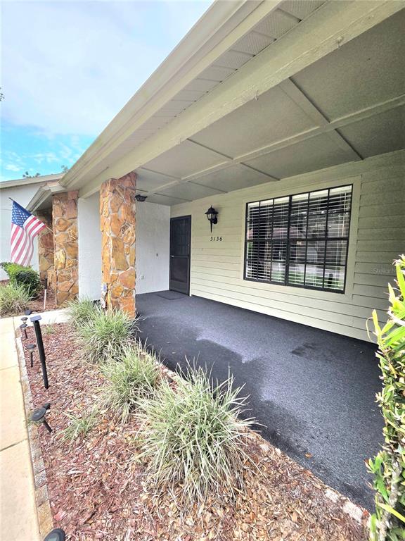 A covered front porch features a stone pillar, horizontal siding, and a dark entry door — 3136 CLOISTER COURT, SPRING HILL, FL