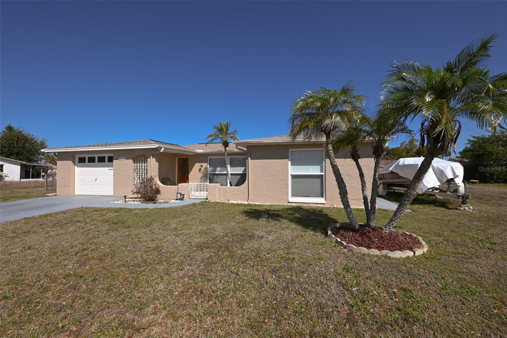 A tan, single-story house with a white garage door and palm trees in the yard — 3233 SALISBURY DRIVE, HOLIDAY, FL