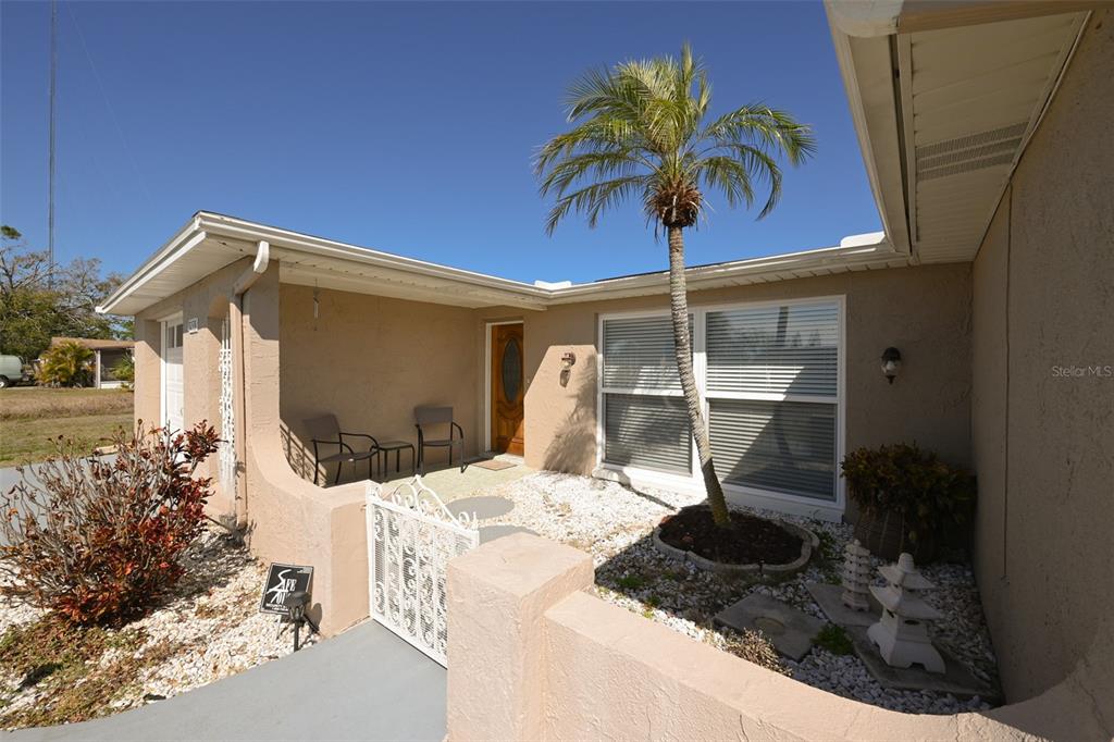 A tan house exterior features a small front porch, a palm tree, and white fencing — 3233 SALISBURY DRIVE, HOLIDAY, FL