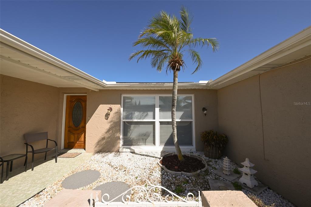 A palm tree stands in a gravel courtyard in front of a house entrance — 3233 SALISBURY DRIVE, HOLIDAY, FL