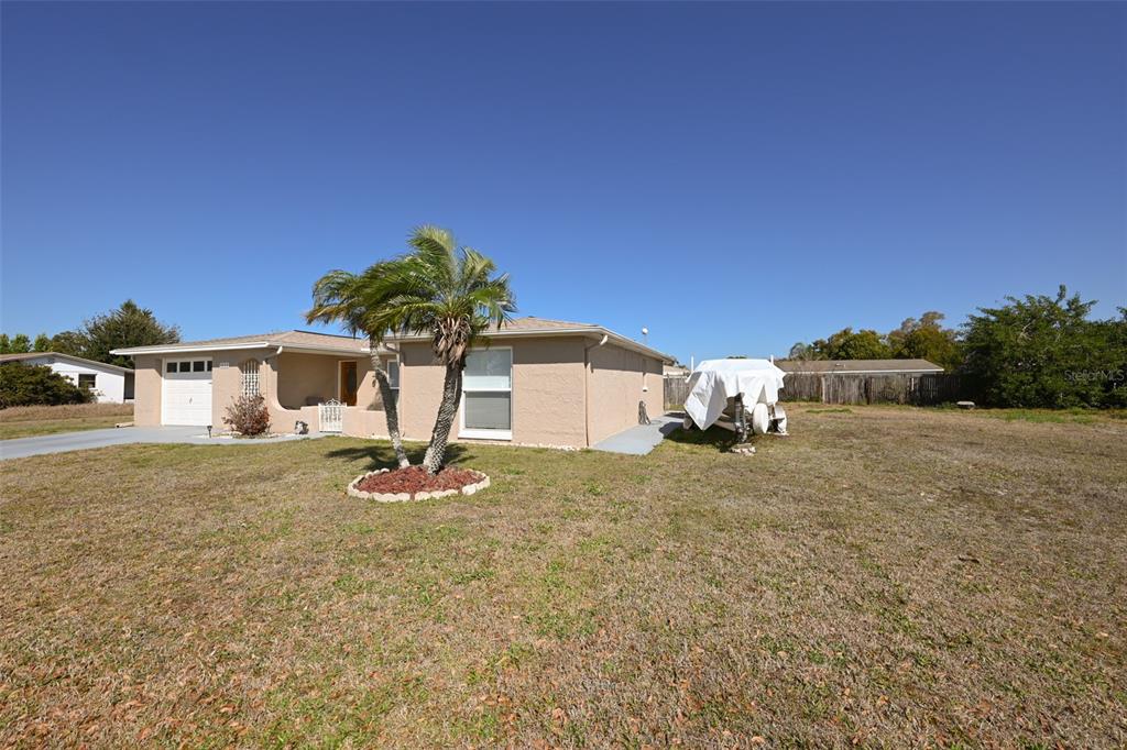 A single-story tan house with a palm tree in the front yard and a boat — 3233 SALISBURY DRIVE, HOLIDAY, FL