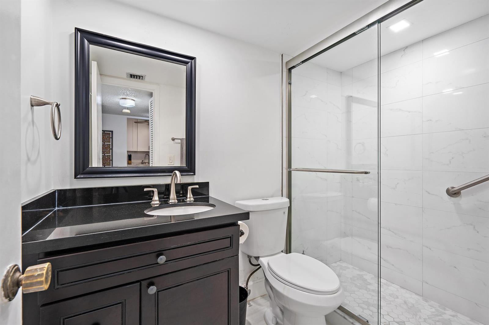A bathroom features a dark wood vanity with a black countertop and a glass shower — 1516 S Lakeside Drive # 207, FL 33460, FL