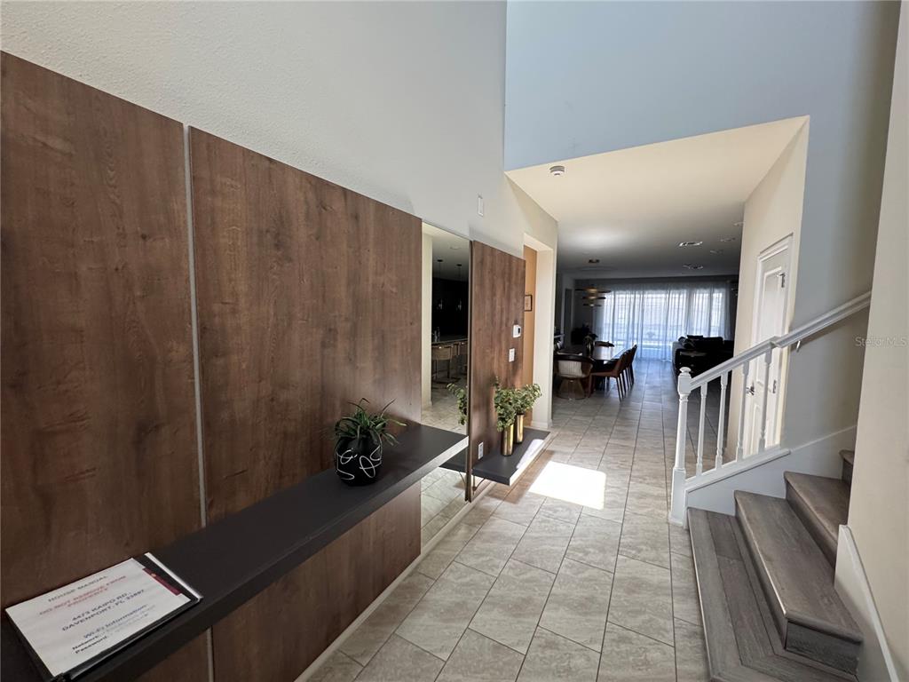 A foyer features wood-paneled walls, a floating shelf, a mirror, and stairs leading upward — 4473 KAIPO ROAD, DAVENPORT, FL