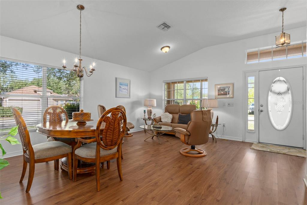 An open-concept dining and living area features wood-look flooring, a chandelier, and a front door — 7228 CRESTED ORCHID DRIVE, BROOKSVILLE, FL