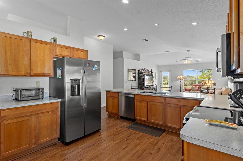 A kitchen with wood cabinets, stainless steel appliances, and a breakfast bar overlooks a living area — 7228 CRESTED ORCHID DRIVE, BROOKSVILLE, FL