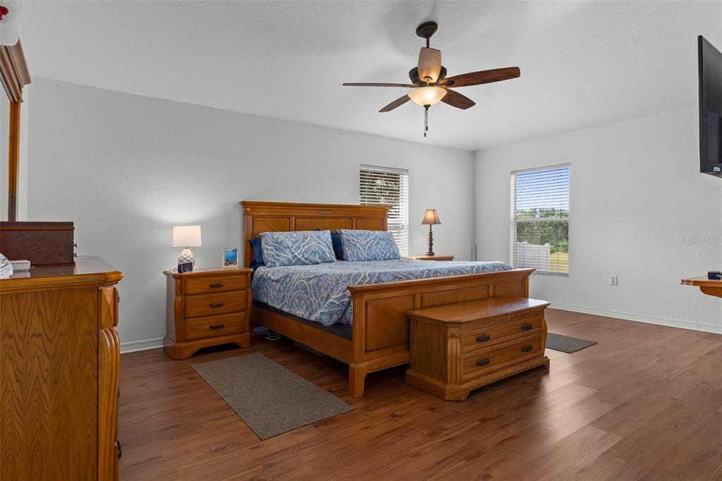 A bedroom features a wooden bed frame, matching furniture, a ceiling fan, and wood-look flooring — 7228 CRESTED ORCHID DRIVE, BROOKSVILLE, FL