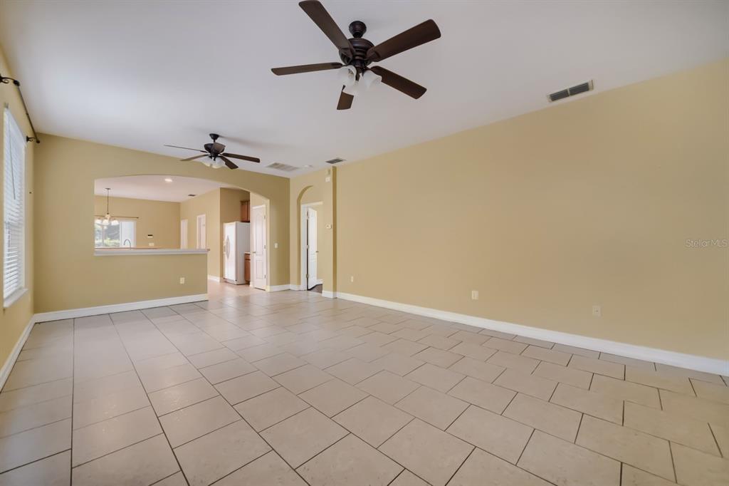 A spacious living room features light-colored tile flooring, beige walls, and two ceiling fans — 3305 BRACKEN FERN DRIVE, HARMONY, FL